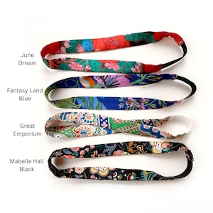 K&ouml;nnte beinhalten: Vier Stoffstirnb&auml;nder mit elastischen B&auml;ndern. Das oberste Stirnband ist rot und gr&uuml;n mit Blumenmustern und als June Dream beschriftet. Das zweite ist blau mit Blumenmustern und als Fantasy Land Blue beschriftet. Das dritte ist gr&uuml;n und wei&szlig; und als Great Emporium beschriftet. Das unterste ist schwarz mit Blumenmustern und als Mabelle Hall Black beschriftet.