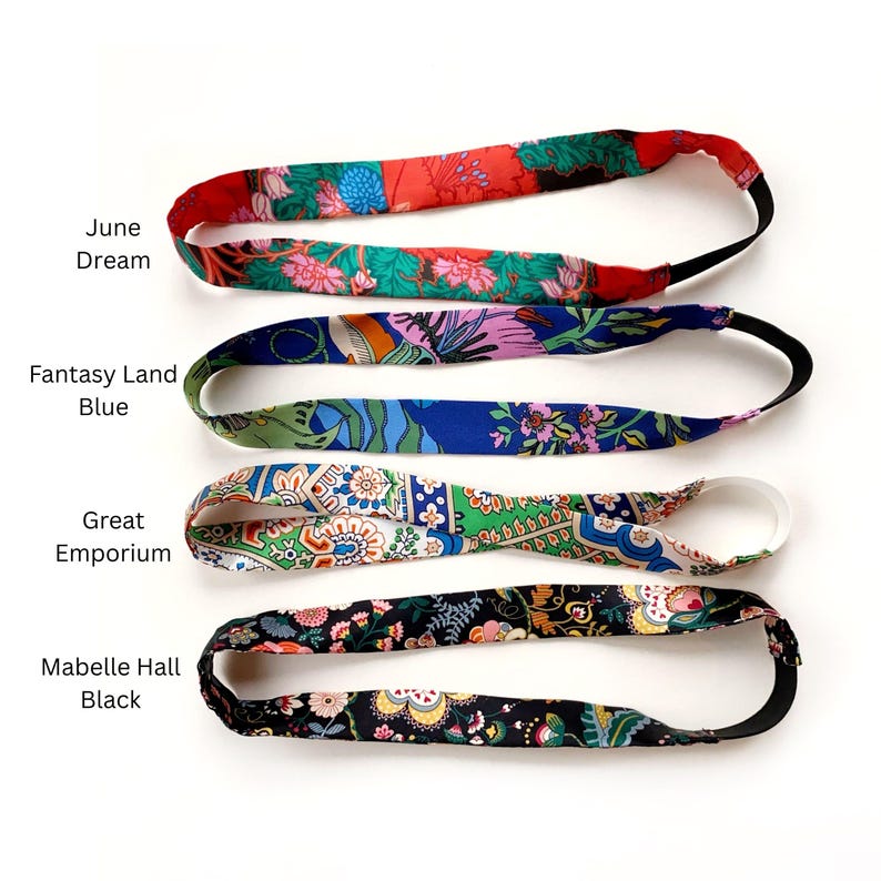 K&ouml;nnte beinhalten: Vier Stoffstirnb&auml;nder mit elastischen B&auml;ndern. Das oberste Stirnband ist rot und gr&uuml;n mit Blumenmustern und als June Dream beschriftet. Das zweite ist blau mit Blumenmustern und als Fantasy Land Blue beschriftet. Das dritte ist gr&uuml;n und wei&szlig; und als Great Emporium beschriftet. Das unterste ist schwarz mit Blumenmustern und als Mabelle Hall Black beschriftet.
