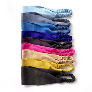 May include: A collection of colorful headbands in various shades, including light blue, gray, blue, purple, brown, pink, beige, yellow, and dark gray. Each headband features a wide, fabric band and an elasticated section for a comfortable fit.