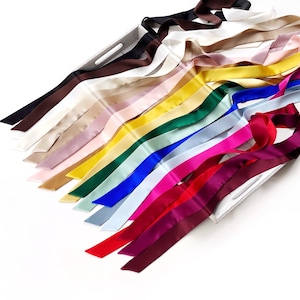 May include: A selection of satin ribbons in a range of colours, including black, brown, white, pink, yellow, green, blue, and red. The ribbons are displayed in a tray, highlighting their smooth texture and vibrant hues.