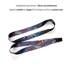 K&ouml;nnte beinhalten: Ein Stoffstirnband mit einem Umfang von 54 cm, das ein sich wiederholendes Muster aus abstrakten t&uuml;rkisfarbenen, violetten und goldenen Formen aufweist. Das Band hat einen schwarzen elastischen Teil. Text: Headband size shown : 54cm circumference.