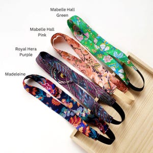 K&ouml;nnte beinhalten: Vier Stoffstirnb&auml;nder mit Gummib&auml;ndern, beschriftet mit Mabelle Hall Green, Mabelle Hall Pink, Royal Hera Purple und Madeleine. Jedes Stirnband weist ein ausgepr&auml;gtes Blumen- oder geometrisches Muster in leuchtenden Farben auf, darunter Gr&uuml;n, Pink, Lila und Marineblau.