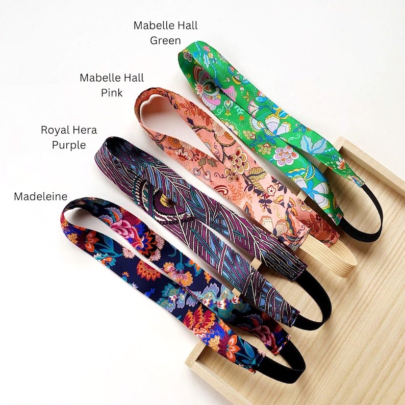 K&ouml;nnte beinhalten: Vier Stoffstirnb&auml;nder mit Gummib&auml;ndern, beschriftet mit Mabelle Hall Green, Mabelle Hall Pink, Royal Hera Purple und Madeleine. Jedes Stirnband weist ein ausgepr&auml;gtes Blumen- oder geometrisches Muster in leuchtenden Farben auf, darunter Gr&uuml;n, Pink, Lila und Marineblau.