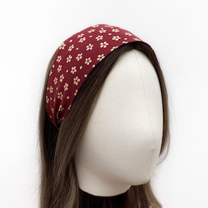 May include: A burgundy headband with a small white floral pattern. The headband is worn on a mannequin with brown hair.