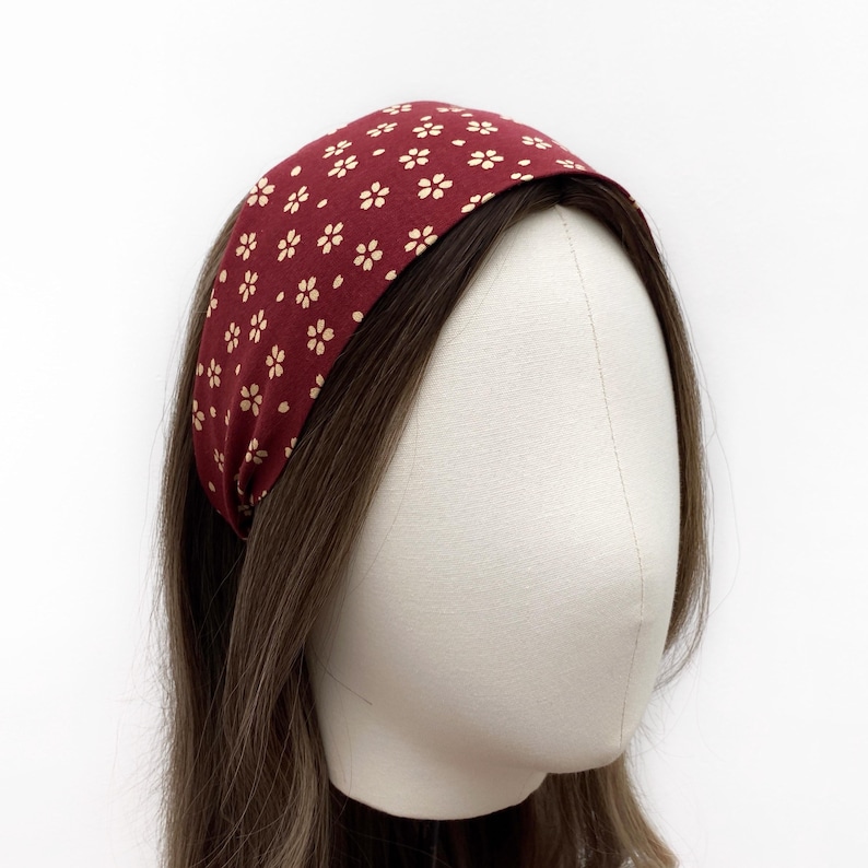 May include: A burgundy headband with a small white floral pattern. The headband is worn on a mannequin with brown hair.