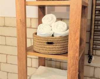 May include: A wooden shelf unit with three shelves, each holding a woven jute basket. The top shelf has an empty basket, the middle shelf has a basket filled with white towels, and the bottom shelf has a stack of white towels.