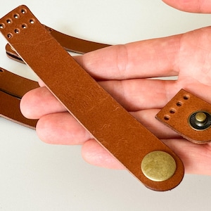 May include: Two brown leather straps with brass buckles and a single brown leather strap with a brass buckle. The straps have holes punched along the edges.