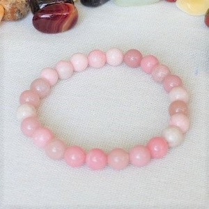 Peut inclure: Un bracelet en pierres précieuses rose et blanc avec des perles rondes. Le bracelet est fait de pierres naturelles et mesure environ 18 cm de long.