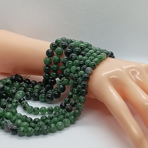 Peut inclure: Un brin de perles de pierres précieuses vertes avec des taches noires et blanches. Les perles sont rondes et lisses, et elles sont enfilées sur un fil transparent.