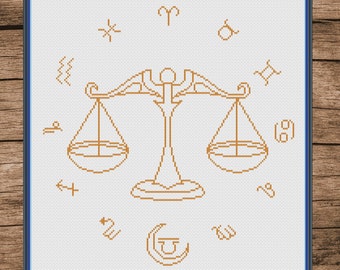 May include: A white cross-stitch pattern with a brown outline of a scale, surrounded by zodiac symbols. The symbols include Aries, Taurus, Gemini, Cancer, Leo, Virgo, Libra, Scorpio, Sagittarius, Capricorn, Aquarius, and Pisces.