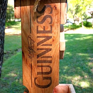 Pode incluir: Um alimentador de p&aacute;ssaros de madeira com um topo preto e uma corda para pendurar. O alimentador &eacute; decorado com o logotipo da Guinness e o texto "Arthur Guinness, Dublin" e "Est. 1759".
