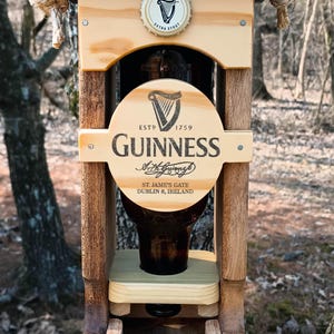 K&ouml;nnte beinhalten: Vogelhaus aus Holz mit einer wiederverwendeten Guinness-Bierflasche. Der Futterspender hat ein schwarzes Dach und eine braune Basis. Das Guinness-Logo ist auf der Flasche und dem Futterspender sichtbar.