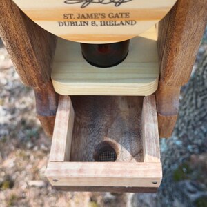 K&ouml;nnte beinhalten: Ein h&ouml;lzerner Vogelh&auml;uschen mit einer kleinen &Ouml;ffnung am Boden. Der Futterspender hat ein Schild mit der Aufschrift "St. Jame's Gate Dublin 8, Ireland".