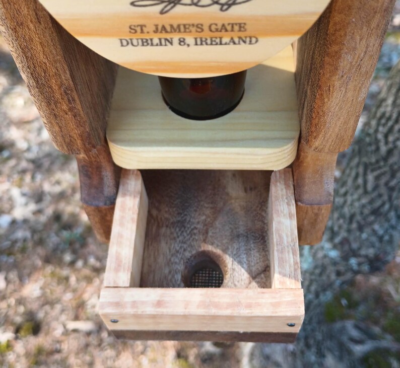 K&ouml;nnte beinhalten: Ein h&ouml;lzerner Vogelh&auml;uschen mit einer kleinen &Ouml;ffnung am Boden. Der Futterspender hat ein Schild mit der Aufschrift "St. Jame's Gate Dublin 8, Ireland".