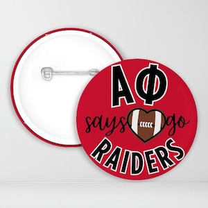 May include: Red and black button with the text "AΦ says go RAIDERS" and a brown football in a heart shape.