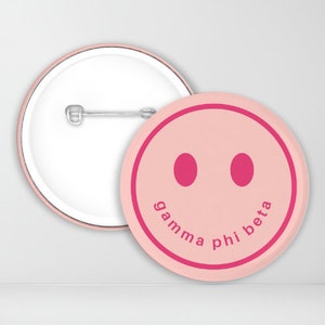 May include: Pink button with a smiling face and the text "gamma phi beta" in pink.