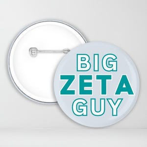 May include: A white button with a blue background and the text "BIG ZETA GUY" in white outlined letters.
