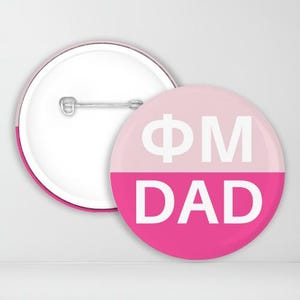 May include: A pink and white button with the text "FM DAD" in white letters.