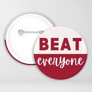 May include: A red and white button with the text "BEAT everyone" in white lettering. The button is a circular shape and has a pin on the back.