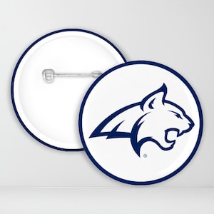 May include: A white button with a blue outline featuring a blue silhouette of a wildcat with a white background. The button has a pin on the back.