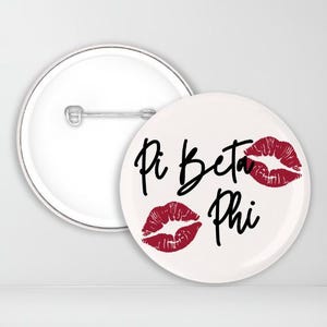 May include: White button with black text that reads "Pi Beta Phi" and three red lips printed on the button.