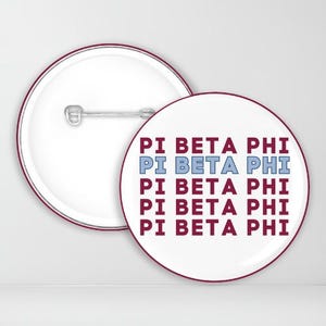 May include: A white button with a maroon border featuring the text "PI BETA PHI" repeated five times in maroon and light blue.
