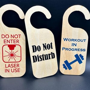 May include: Three wooden door hangers with curved tops. One reads "DO NOT ENTER" with a red laser graphic, another says "Do Not Disturb", and the last says "WORKOUT IN PROGRESS" with a blue dumbbell.