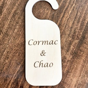 May include: A white wooden door hanger with the text "Cormac & Chao" engraved on it.