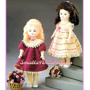 May include: Two crocheted doll dresses, one in a burgundy color and the other in a cream color with pink stripes. The dolls are wearing the dresses and are standing on a set of stairs. The doll in the burgundy dress is holding a basket of pink flowers.