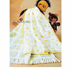 May include: A white crochet baby blanket with a yellow border and a daisy pattern. The blanket is draped over a rocking horse and a teddy bear.