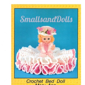 以下が含まれることがあります： 「メアリー・アン」という名前の、白地にピンクの縁取りのドレスを着た、ピンクの花のついた白い帽子をかぶった、かぎ針編みのベッドドール。ドールは白とピンクのかぎ針編みのスカートに座っています。