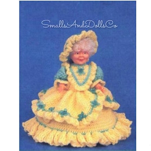 May include: Crochet doll dress pattern for a small doll. The dress is yellow with green trim and a white crocheted hat. The pattern is from Smalls And Dolls Co.