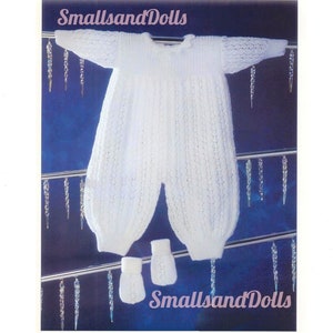 May include: White knitted baby outfit with matching booties. The outfit is a one-piece with long sleeves and a lace pattern. The booties are also knitted with a lace pattern. The outfit is hanging on a hanger with icicle decorations.