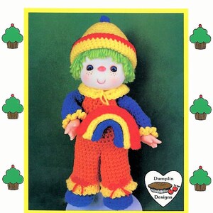 May include: Crochet pattern for a rainbow slush doll. The doll is wearing a yellow and red hat, a blue and yellow shirt, and orange pants. The doll is holding a rainbow in its hands. The pattern is from "Cupcake Corner".