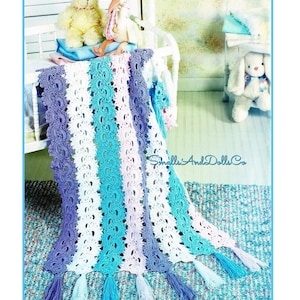 Pode incluir: Um cobertor de bebê de crochê feito à mão em tons de azul, branco e lavanda. O cobertor apresenta listras verticais e borlas decorativas ao longo da borda inferior. O texto "Small's And Dolls Co" é visível.