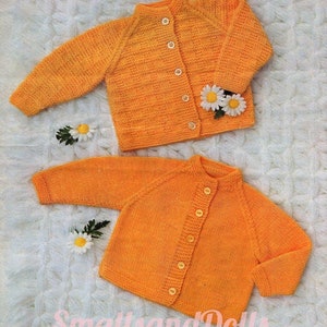May include: Two orange knitted baby cardigans with button closures. The top cardigan has a textured pattern. Both cardigans are laid out on a white fuzzy surface.