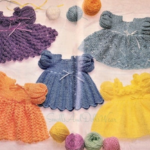 Może przedstawiać: Pięć szydełkowych sukienek dla lalek w kolorze fioletowym, niebieskim, jasnoniebieskim, pomarańczowym i żółtym. Sukienki są wykonane z delikatnym wzorem koronkowym i mają falbankę. Sukienki są ułożone na białym tle z kłębkami włóczki i wstążką.