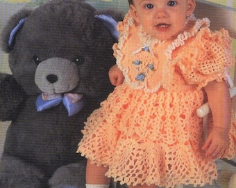 May include: A baby girl wearing a peach crocheted dress with a white crocheted collar and a blue bow. She is sitting on a white rocking chair with a gray teddy bear beside her.