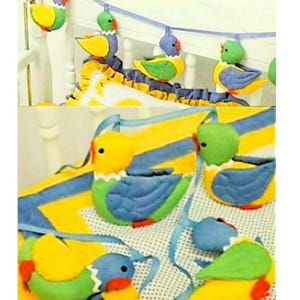 May include: A set of colorful, felt bird toys with yellow, green, and blue accents. The birds are strung together with a blue ribbon and can be hung from a crib or playpen.