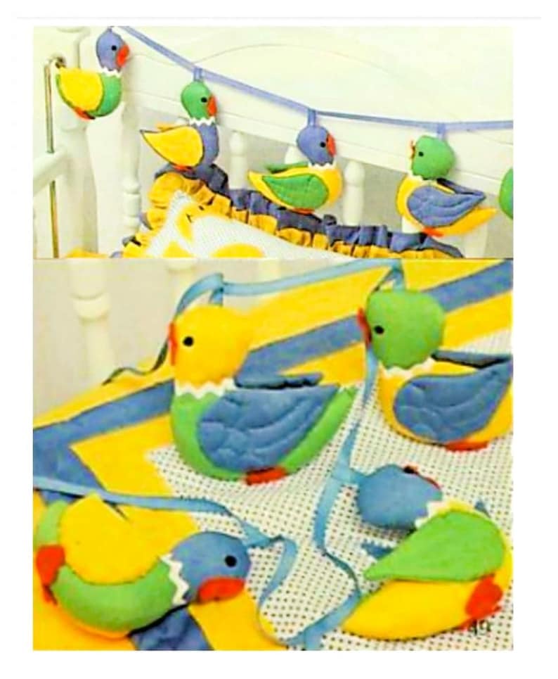 May include: A set of colorful, felt bird toys with yellow, green, and blue accents. The birds are strung together with a blue ribbon and can be hung from a crib or playpen.