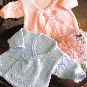 May include: Two knitted baby sweaters, one pink and one light blue, with a lace pattern and a bow tie closure.