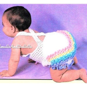 Könnte beinhalten: Ein Baby trägt ein weißes gehäkeltes Oberteil mit einem Regenbogen-Rüschenbesatz. Das Oberteil hat einen Kreuzriemen-Design im Rücken.