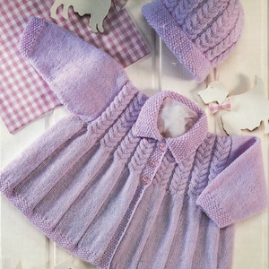 May include: A lavender knitted baby jacket with a cable knit pattern and a matching hat. The jacket has a button closure and a collar.