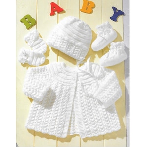 May include: A white knitted baby outfit set including a cardigan, hat, and booties. The set is laid out on a wooden surface with the word "BABY" spelled out in colourful letters.