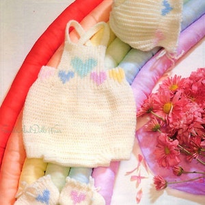 May include: A set of crocheted baby clothes in white with pastel pink, blue, and yellow hearts. The set includes a hat, a sleeveless top, and booties.