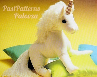May include: A white plush unicorn toy with a gold and white horn, sitting on a green and yellow pillow. The unicorn has a long white mane and tail.