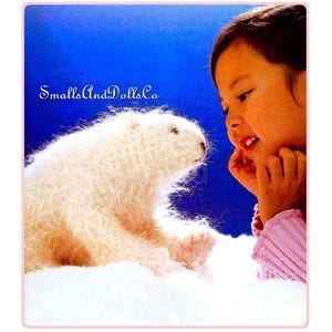 May include: A white crocheted polar bear plush toy sits on a white fluffy surface, looking at a young girl with a pink sweater. The girl is smiling and looking at the bear. The background is a bright blue.