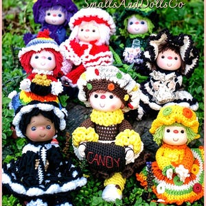 May include: A collection of seven handcrafted crochet dolls featuring various colorful outfits, hats, and accessories. One doll holds a black basket with the word CANDY embroidered in red. The dolls have painted faces and are arranged together.