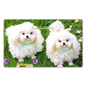 May include: Two handmade crochet Pekingese dog figures made of off-white yarn with long, shaggy fur, black plastic eyes, and black stitched noses. Each figure features a light green ribbon tied around its neck. Text reads SmallsAndDollsCo and Pekingese.