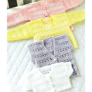 May include: Four crocheted baby sweaters in different colors: pink, yellow, purple, and white. Each sweater has a button closure and a delicate openwork pattern.
